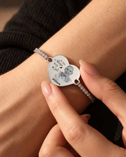 Fingertoppar som håller det graverade hjärtat med bild på det silverfärgade tennisarmbandet