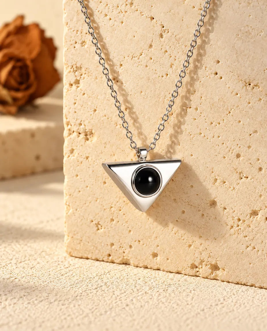 Personligt silverfärgat triangelhalsband med bild inuti, hängande på ett block av travertin
