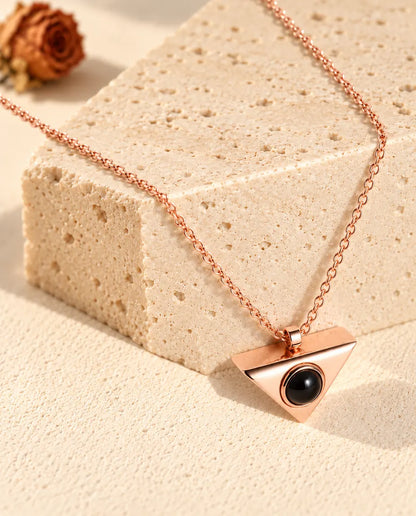 Roséguldfärgat triangelhalsband med bild inuti, hängande över ett block av travertin