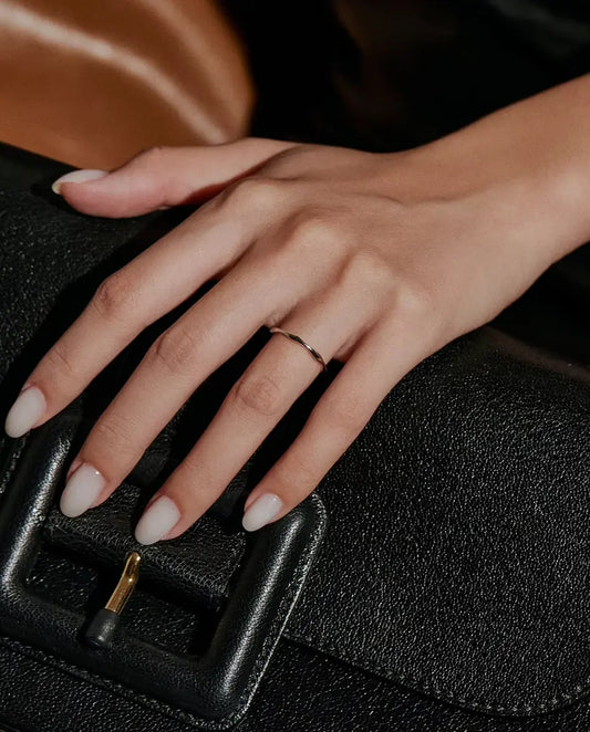 Vågig Ring i 925 Sterlingsilver - buren på en hand som vilar på en svart väska