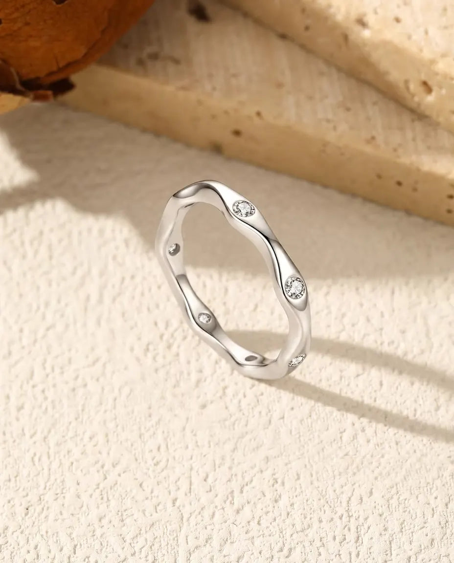 Vågig Moissanite Ring i 925 Sterlingsilver - stående på en ljus strukturerad yta
